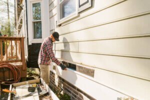 Construction worker repairing a colonial style house siding Siding Contractor project by U.S. Windows & Exteriors for a residential home in Kennesaw, GA